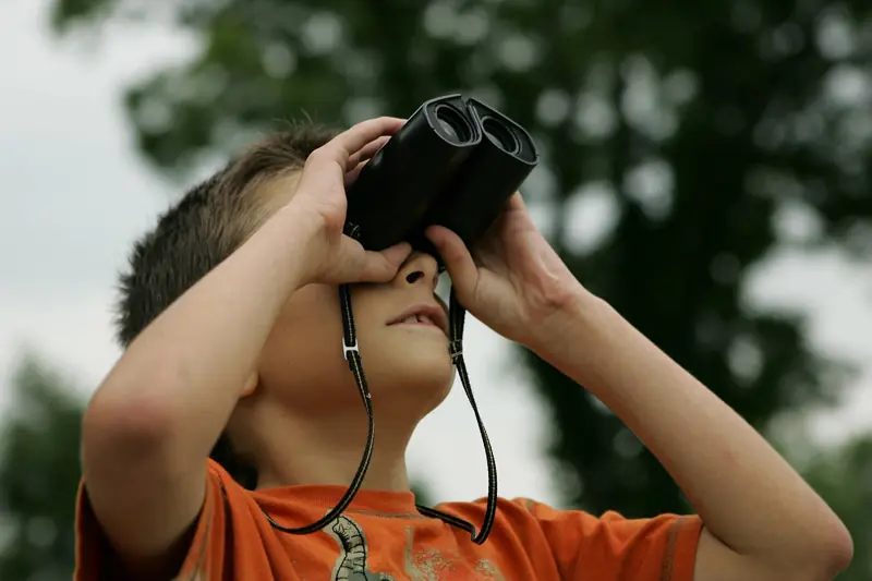 Child looking up through binoculars outdoors